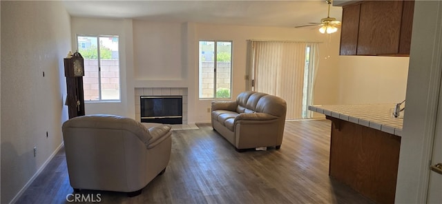 living room featuring ceiling fan, a tiled fireplace, dark hardwood / wood-style floors, and a healthy amount of sunlight