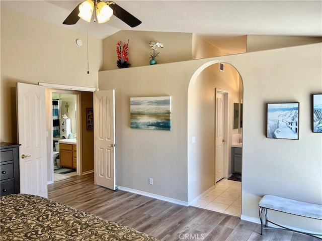 bedroom featuring light wood-type flooring, ensuite bathroom, ceiling fan, and lofted ceiling