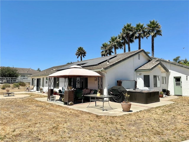 rear view of property with outdoor lounge area, solar panels, a yard, a patio area, and a hot tub