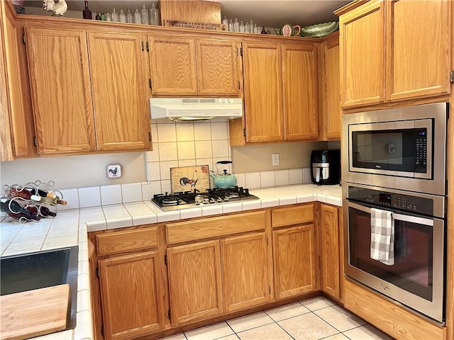 kitchen with tile counters, light tile patterned flooring, appliances with stainless steel finishes, and tasteful backsplash