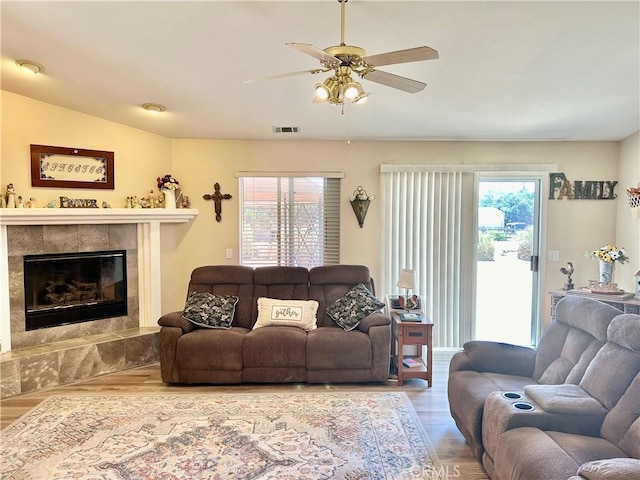 living room with a tile fireplace, a wealth of natural light, ceiling fan, and wood-type flooring