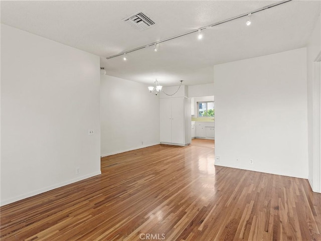 spare room with an inviting chandelier, rail lighting, and hardwood / wood-style flooring