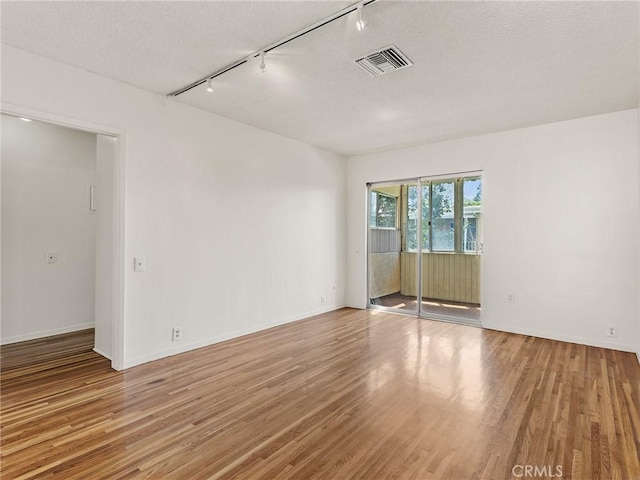 unfurnished room with a textured ceiling, light hardwood / wood-style floors, and track lighting