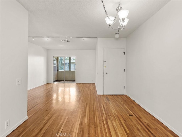 empty room featuring a textured ceiling, rail lighting, a notable chandelier, and light wood-type flooring