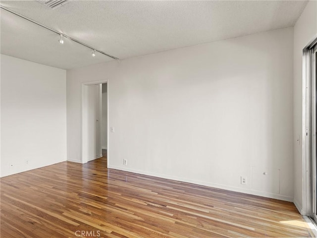 spare room with a textured ceiling, light wood-type flooring, and rail lighting