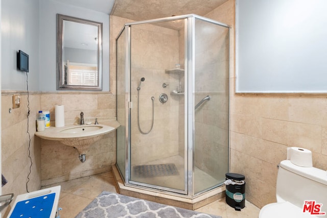 bathroom with tile patterned floors, a shower with door, sink, tile walls, and toilet