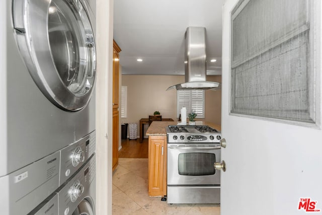 kitchen with gas range, wall chimney range hood, light stone counters, stacked washer / drying machine, and light tile patterned flooring