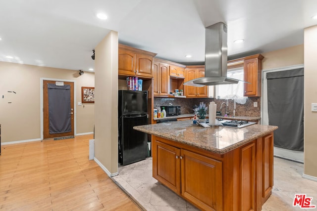 kitchen with a center island, dark stone counters, black appliances, tasteful backsplash, and island range hood