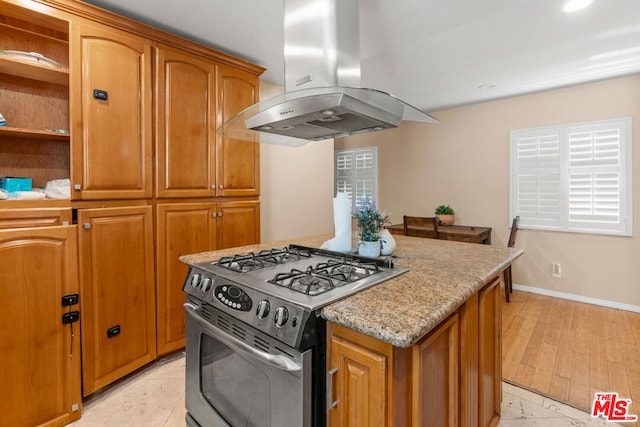 kitchen with stainless steel gas range oven, light stone countertops, light hardwood / wood-style floors, and island exhaust hood