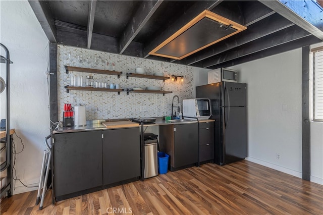 kitchen featuring dark hardwood / wood-style flooring, stainless steel counters, sink, and black refrigerator