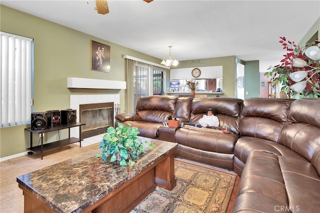 living room with ceiling fan with notable chandelier, a tiled fireplace, and light tile patterned floors