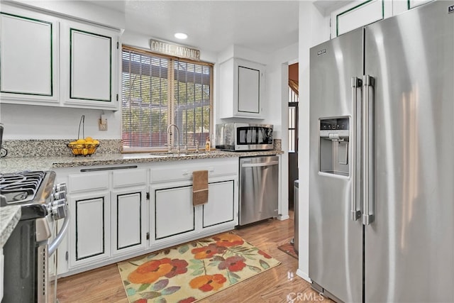 kitchen with appliances with stainless steel finishes, light hardwood / wood-style floors, sink, and white cabinets