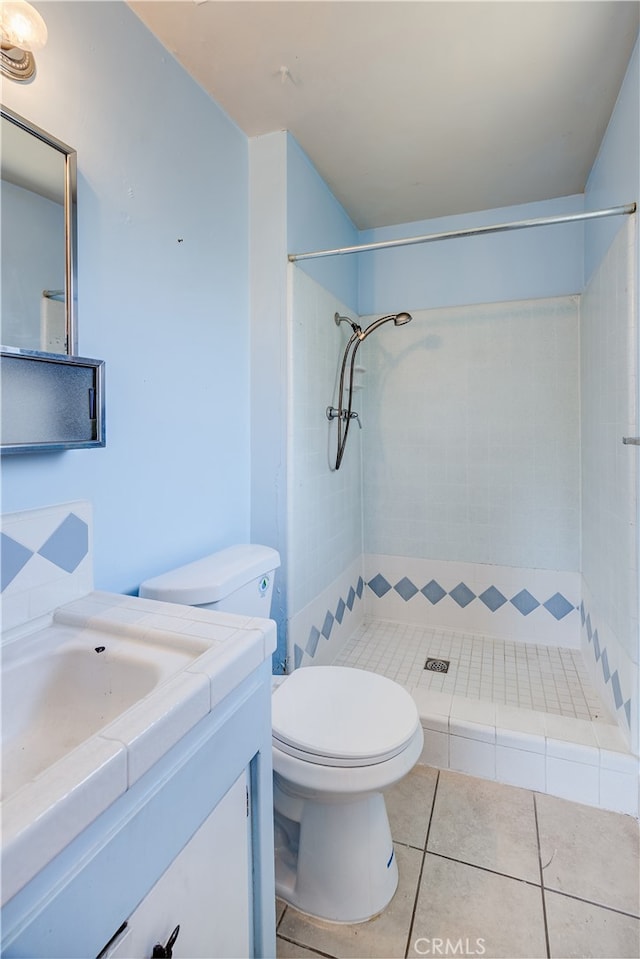 bathroom featuring vanity, a tile shower, toilet, and tile patterned floors