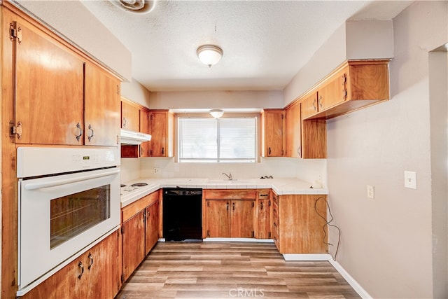 kitchen with a textured ceiling, light wood-type flooring, tile counters, sink, and white appliances