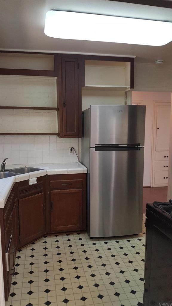 kitchen featuring stainless steel refrigerator, sink, black range with electric cooktop, tile counters, and decorative backsplash