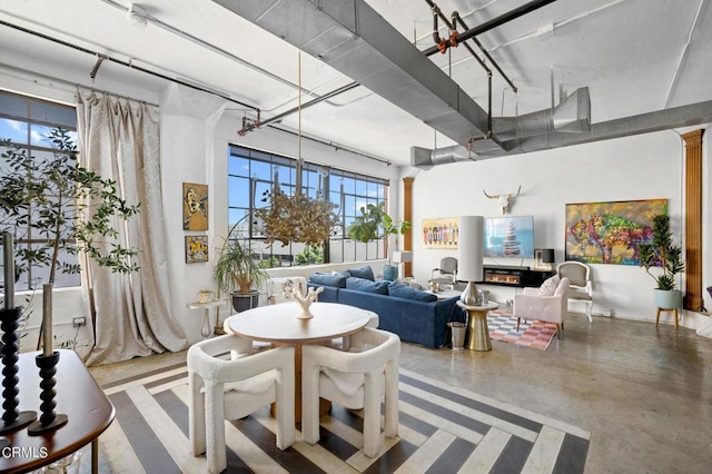 dining room featuring concrete floors, decorative columns, and a high ceiling