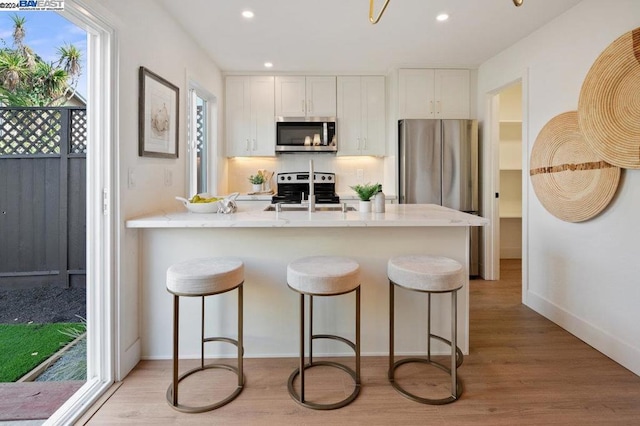 kitchen featuring a breakfast bar, stainless steel appliances, light wood-type flooring, and white cabinetry