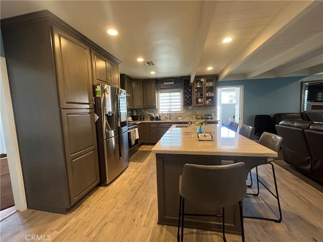 kitchen featuring light hardwood / wood-style flooring, stainless steel fridge, tasteful backsplash, dark brown cabinets, and a kitchen bar