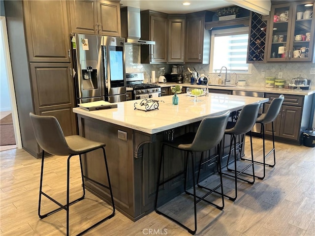 kitchen with a breakfast bar area, wall chimney exhaust hood, light hardwood / wood-style floors, a kitchen island, and stainless steel appliances