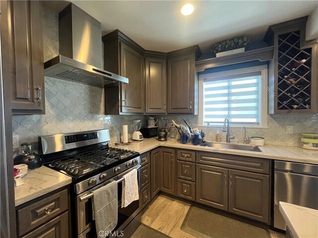 kitchen with sink, stainless steel appliances, tasteful backsplash, and wall chimney range hood