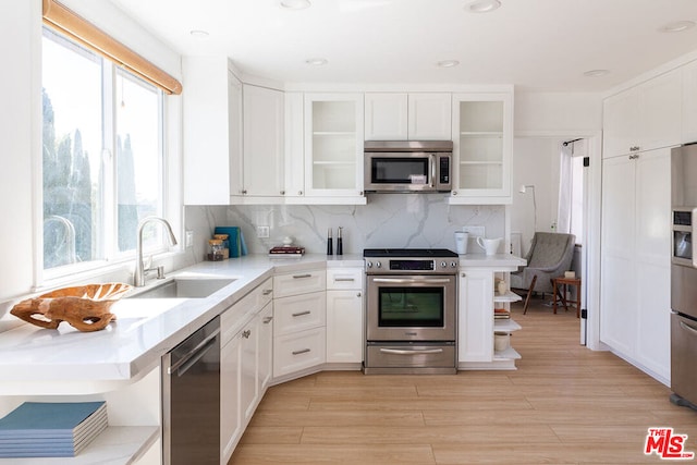 kitchen with sink, light hardwood / wood-style flooring, backsplash, white cabinets, and appliances with stainless steel finishes