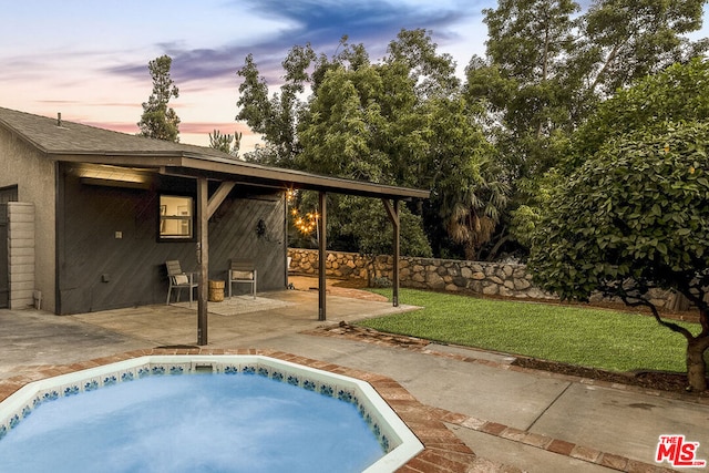 pool at dusk featuring a hot tub, a patio area, and a lawn