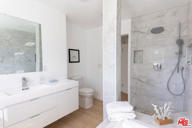 bathroom featuring a tile shower, toilet, vanity, and hardwood / wood-style flooring