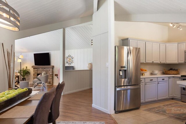 kitchen featuring wooden walls, vaulted ceiling with beams, light wood-type flooring, a fireplace, and appliances with stainless steel finishes