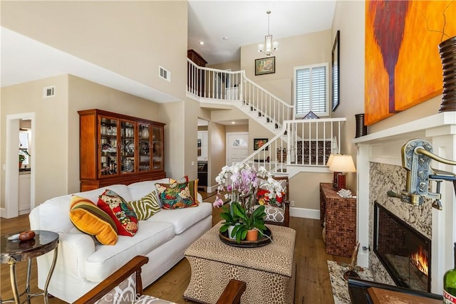 living room featuring dark wood-type flooring, a premium fireplace, a towering ceiling, and an inviting chandelier