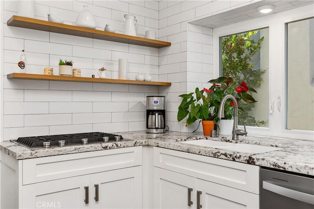 kitchen with white cabinets, appliances with stainless steel finishes, decorative backsplash, sink, and light stone counters