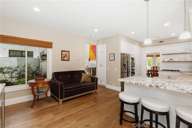 kitchen featuring light stone countertops, decorative light fixtures, white cabinetry, stainless steel appliances, and light hardwood / wood-style floors