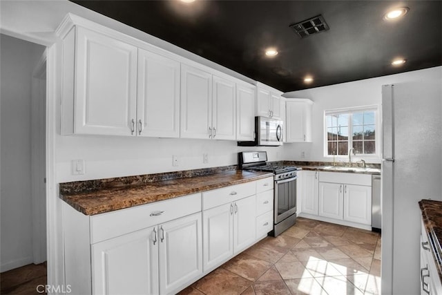 kitchen featuring white cabinets, light tile patterned floors, stainless steel appliances, dark stone counters, and sink