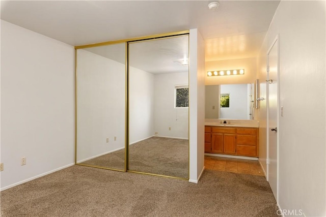 unfurnished bedroom with ensuite bath, light carpet, a closet, and sink