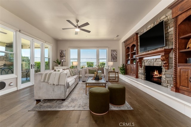 living room with dark wood-type flooring, ceiling fan, built in features, and a fireplace