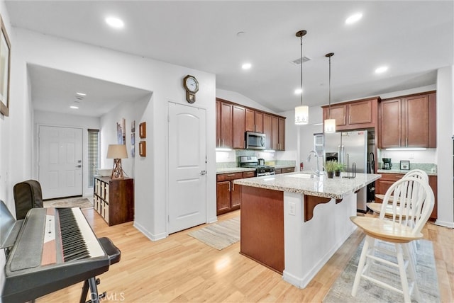 kitchen featuring an island with sink, stainless steel appliances, light hardwood / wood-style flooring, decorative light fixtures, and sink