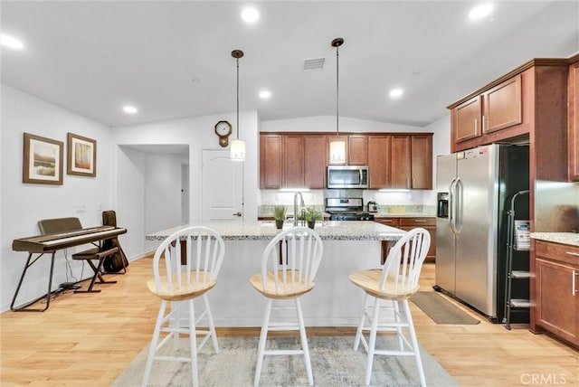 kitchen featuring pendant lighting, lofted ceiling, appliances with stainless steel finishes, and light stone counters