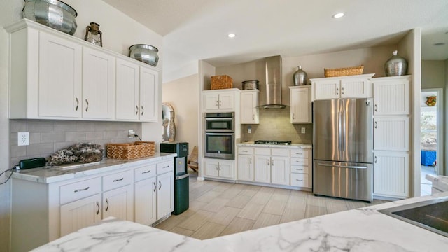 kitchen featuring appliances with stainless steel finishes, wall chimney exhaust hood, white cabinetry, tasteful backsplash, and light stone counters