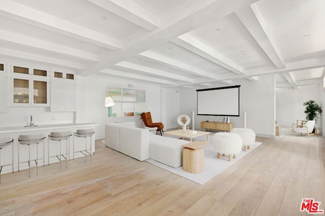 home theater with beamed ceiling, light wood-type flooring, and sink