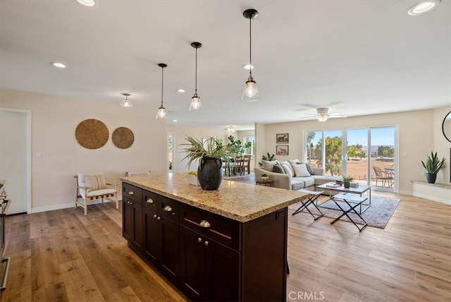 kitchen featuring dark brown cabinets, a center island, pendant lighting, light wood-type flooring, and light stone counters