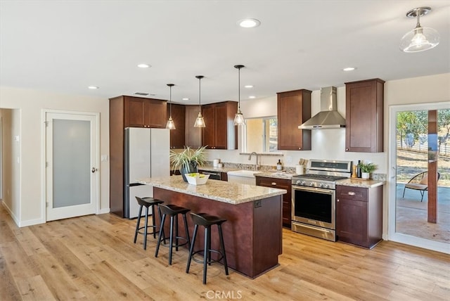 kitchen featuring a kitchen island, stainless steel range with gas stovetop, light hardwood / wood-style floors, wall chimney exhaust hood, and white refrigerator