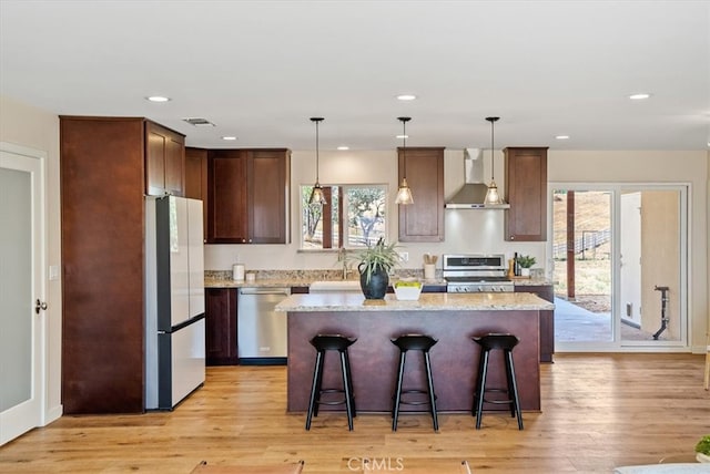 kitchen with light stone counters, a kitchen island, light hardwood / wood-style floors, wall chimney exhaust hood, and stainless steel appliances