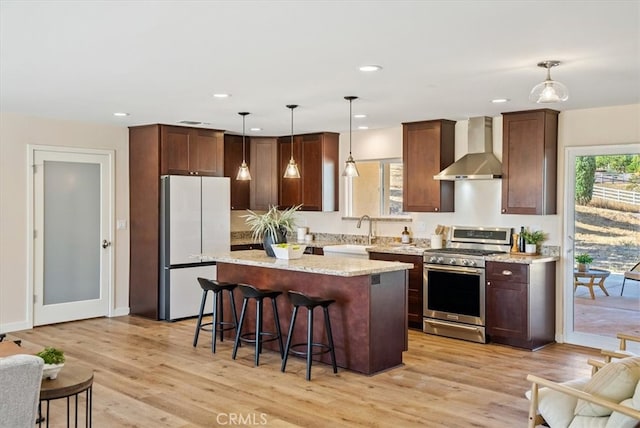 kitchen with wall chimney range hood, gas stove, hanging light fixtures, light hardwood / wood-style floors, and white fridge