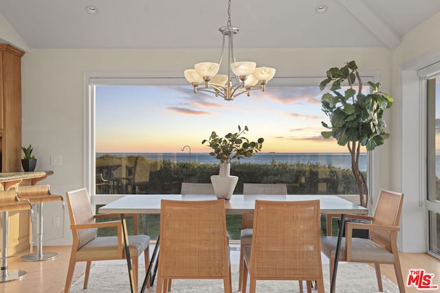 dining area with a water view, a chandelier, and vaulted ceiling