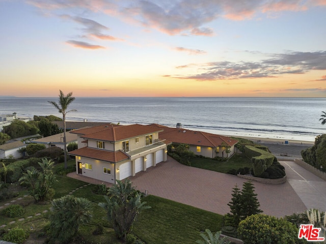 aerial view at dusk featuring a water view and a beach view