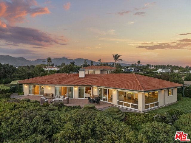 back house at dusk featuring a mountain view, outdoor lounge area, and a patio