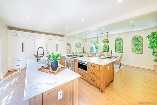 kitchen with white cabinetry, light stone counters, pendant lighting, a spacious island, and light hardwood / wood-style floors