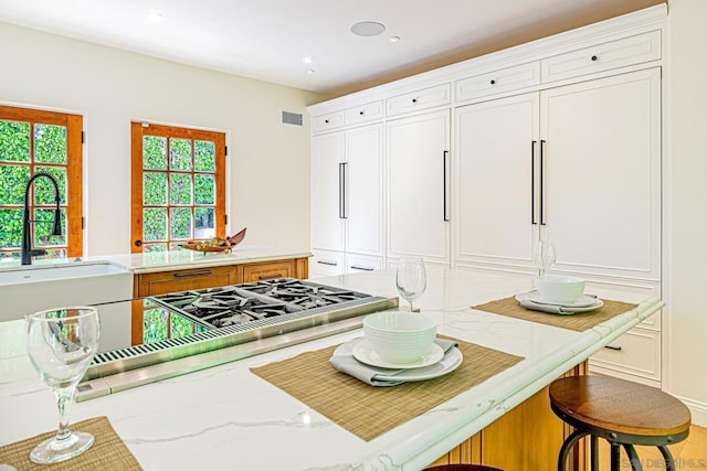 kitchen featuring light stone countertops, sink, a kitchen breakfast bar, kitchen peninsula, and white cabinets