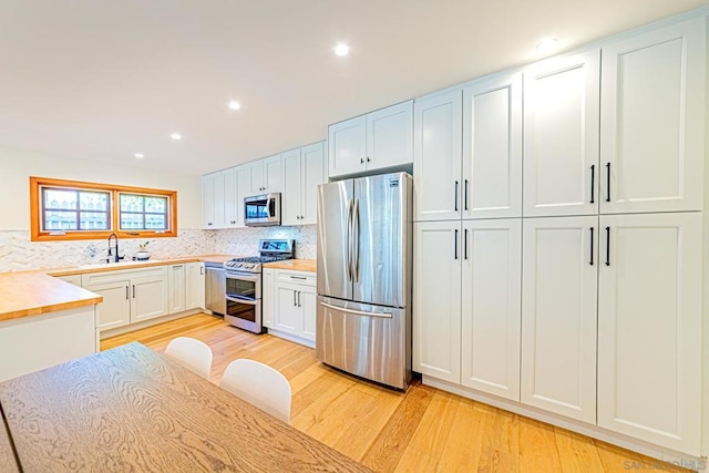 kitchen with appliances with stainless steel finishes, light wood-type flooring, backsplash, sink, and white cabinetry