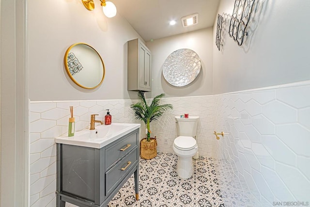 bathroom featuring vanity, toilet, and tile walls