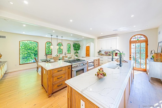 kitchen featuring stainless steel stove, light stone counters, a spacious island, light hardwood / wood-style floors, and white cabinets